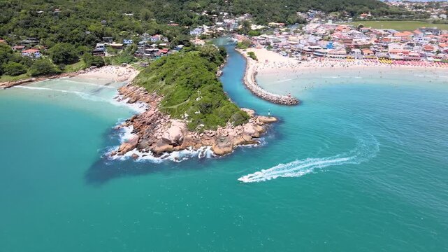 Panoramic aerial view of Barra da Lagoa Beach in Florian&oacute;polis Santa Catarina Brazil with yacht sailing in turquoise blue sea on a sunny summer day with the beach crowded with people.