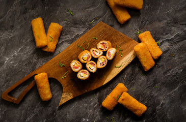 Flat lay of sliced risoles mayo on a wooden board over dark marble. Crispy Indonesian snack with egg and smoked beef or chicken filling. Ideal for banner, menu header, or food blog.