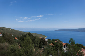 Fototapeta premium Scenic view of the Adriatic Sea with red-roof houses in a coastal Croatian village under a clear blue sky. Peaceful seascape with gentle waves and wide horizon under a clear sky in Croatia.
