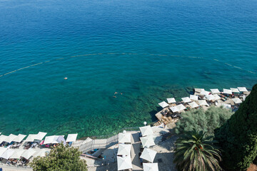 Aerial view of Opatija beach in Croatia with turquoise Adriatic Sea, white parasols, sunbeds, and swimmers enjoying a sunny summer. Scenic seaside resort in Opatija, Croatia, clear blue water.