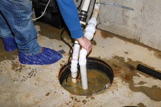   A plumber repairing a sump pump in a flooded basement in a residential home