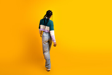 Naklejka premium Stylish young woman in casual attire walking against a vibrant yellow background showcasing modern fashion and confidence