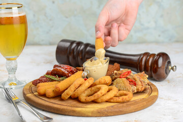 set of beer snacks on a wooden board with sauce on a light background with human hands