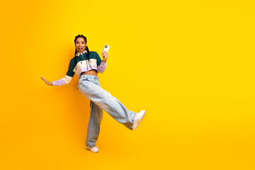 Obraz premium Vibrant young woman holding a smartphone showcasing joyful energy and modern style against a vivid yellow background