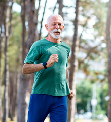 Obraz premium Smiling active mature elderly man jogging running in the park