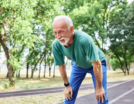 Portrait of a mature senior man exercising in a park, tired mature male running and taking a break outdoors, healthy lifestyle and cardio exercise in nature concepts, vitality and active senior - Powered by Adobe