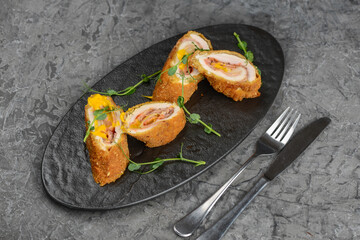 chicken rolls with filling in a black plate on a gray concrete background macro