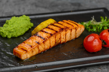 grilled salmon fillet in a black plate with tomatoes on a gray concrete background macro