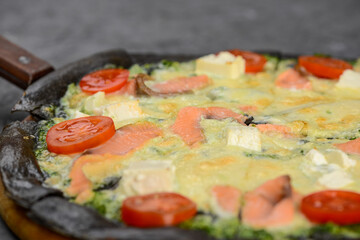 pizza with black dough with fish and tomato filling with cheese on a gray background macro photo