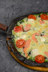 pizza with black dough with fish and tomato filling with cheese on a gray background macro 