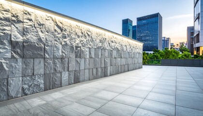 Fototapeta premium A modern urban plaza, featuring a light-toned stone wall and paved floor, stretches towards a backdrop of high-rise buildings against a clear twilight sky.