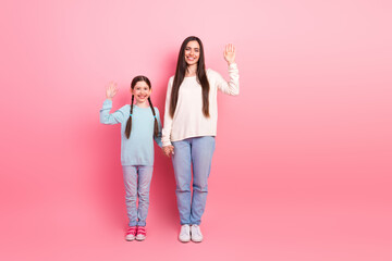 Fototapeta premium Mother and daughter holding hands and waving on a pink background, emphasizing love, joy, and family togetherness