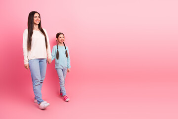 Happy mother and daughter walking hand in hand, smiling together against pink background, enjoying quality bonding time