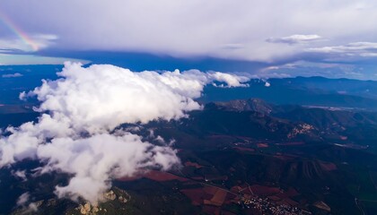 High-altitude view of dramatic cloudscape over a mountainous terrain, showcasing a vibrant rainbow.