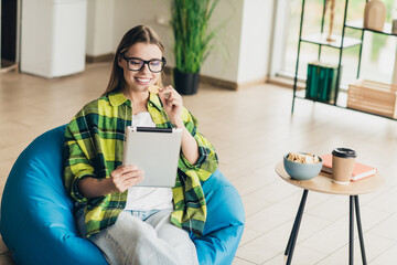 Young woman enjoying leisure time, sitting comfortably indoors, browsing on tablet and enjoying snacks in casual style