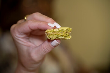 main d'une femme tenant un macaron à la pistache dans lequel elle a croqué