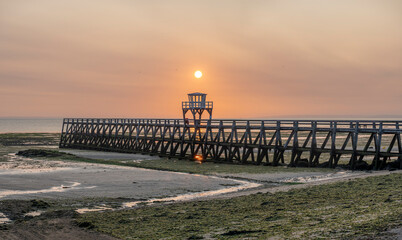 Luc-Sur-Mer, France - 08 10 2025: Panoramic view of the wooden pier in front of the sea named Fisherman's Pier at sunrise with the sun rising and Le Havre far away behind