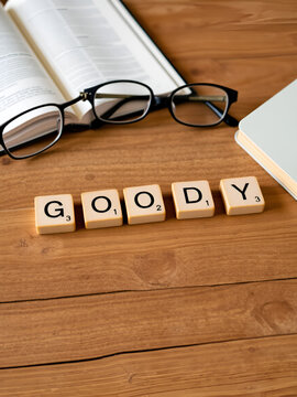 goody word or concept represented by wooden letter tiles on a wooden table with glasses and a book