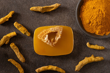 Turmeric soap bar and powder turmeric root on dark brown background. Organic skincare product perfect for wellness, beauty, and organic body care concepts. View from above.