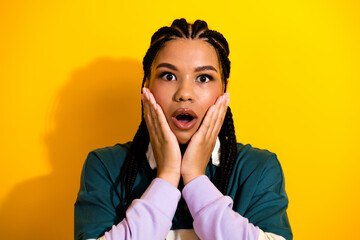 Studio portrait of a young woman with braids on a yellow background expressing astonishment with a...