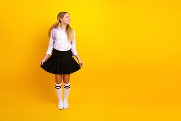 Teen schoolgirl standing confidently in uniform against yellow background, striking a cheerful pose, ready for back to school activities