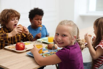 Little kids eating lunch at wooden table in school canteen