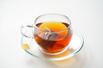 Glass cup of hot black and herbal tea with a slice of lemon on a white saucer