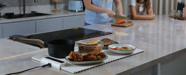 A person is cutting a carrot on a kitchen counter behind a white food-warming mat that holds a...