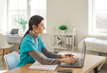 Nurse, young female doctor using laptop online, writing notes in medical journal sitting at desk, professional medic physician working on computer at workplace, med student learning, planning 
