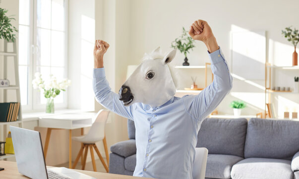 Funny extravagant happy man wearing donkey, horse head happy celebrating near laptop online showing impressive achievements, lottery winner, successful deal, excessively wealth, cute amuse guy playing