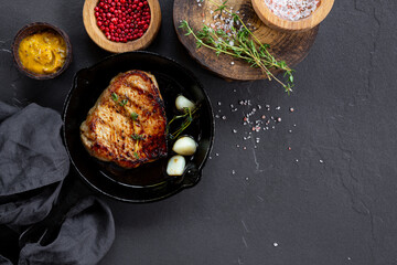Grilled pork chop in black frying pan on dark background, meat top view copy space for text