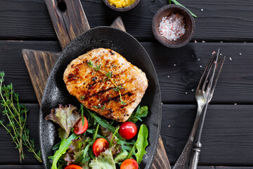 Grilled pork chop with fresh salad in black plate on black background, meat top view