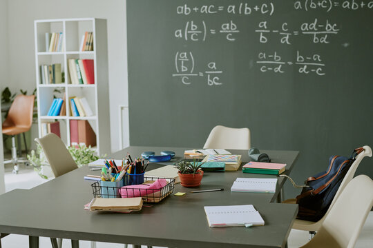 Empty classroom showing modern desks with school supplies, notebooks, and backpack in foreground, chalkboard with algebra equations in background, no people visible - Powered by Adobe