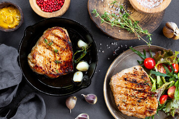 Grilled pork chop in black frying pan and plate on black background, meat top view