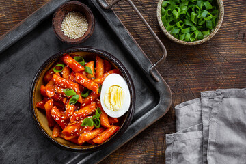 Korean street food, tteokbokki with egg and sesame in a bowl on dark wooden background top view