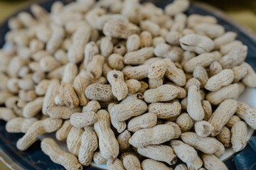 Close-up of raw peanuts in shells arranged on a plate. Natural dry peanut pods with rough textured shells, perfect for illustrating organic food, agriculture, healthy snacks, legumes, and traditional 