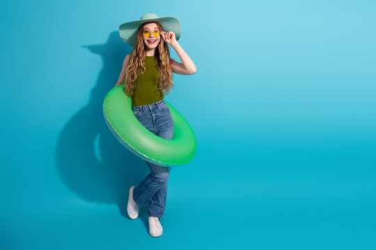 Fashionable young woman with green inner tube and sunglasses enjoying summer against bright blue background