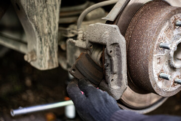 A gloved hand removes a worn brake pad from a car caliper in preparation for replacing it