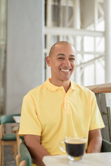 Mature Hispanic bald man sitting at a cafe while enjoying a coffee break