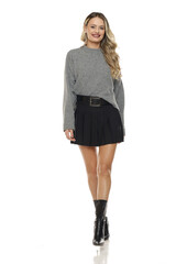 Studio full body shot of blonde woman in gray sweater, black skirt and boots walking and smiling on studio white background.
