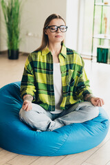 Obraz premium Young woman meditating on bean bag in casual interior, exhibiting mindfulness while balancing professional and leisure pursuits