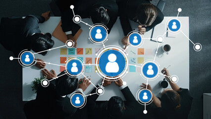 A high-angle view of a diverse team engaged in a collaborative discussion, showcasing digital connections and networking, emphasizing teamwork and idea-sharing in a modern office setting. Amity