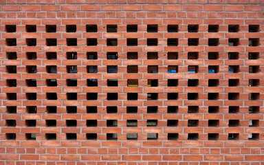 perforated red brick wall with evenly spaced square openings, allowing glimpses of the interior behind it