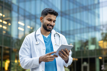 Smiling doctor using a tablet in front of the hospital