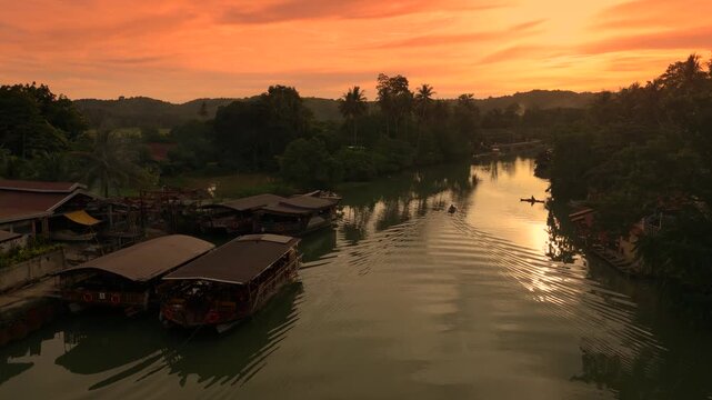 Aerial of a small boat with a man paddling at sunset. Docked tour boats and green trees line the banks of the Amazon River.