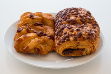 Dolci di pasta sfoglia con noci pecan e al cioccolato su piattino bianco