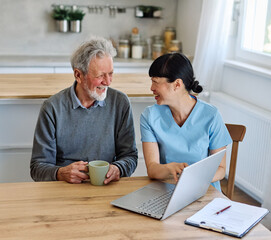 Female caregiver with senior woman and man using laptop at home