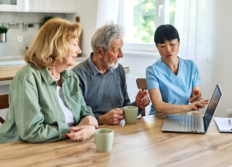 Female caregiver with senior woman and man using laptop at home