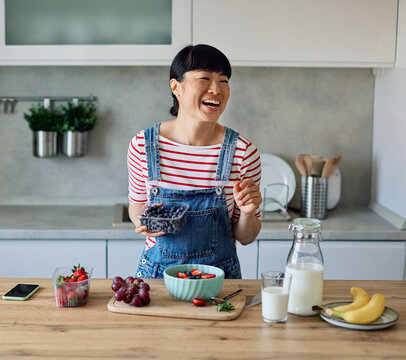 Portrait of a healthy young asian woman enjoying delicious fruit and cereal salad breakfast bowl at home - Powered by Adobe