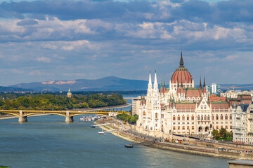 Obraz premium View from Castle Hill of Danube River with shining neo-Gothic Parliament building, Margaret Island's art nouveau water tower, and distant hills under blue autumn sky. Budapest, Hungary.
